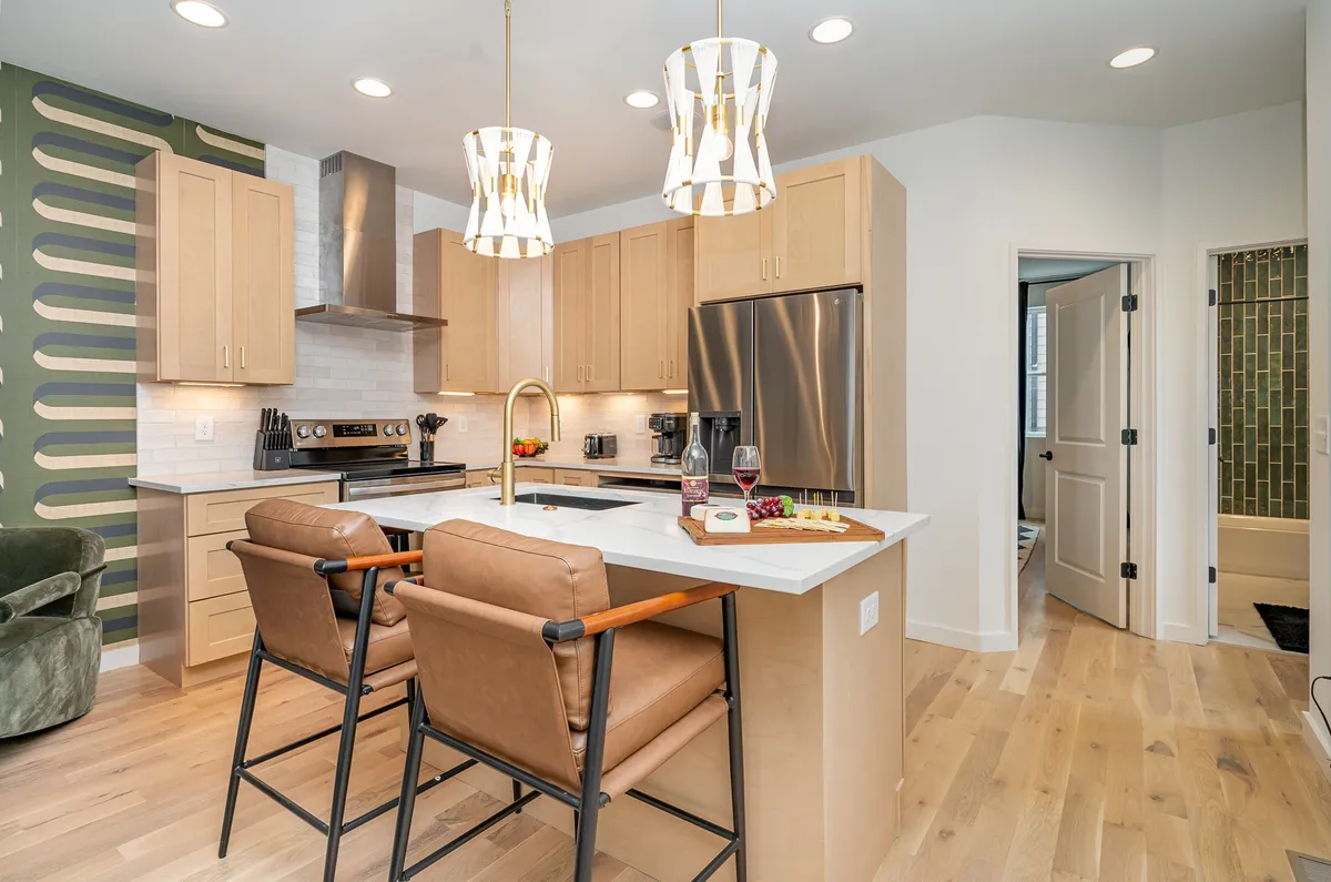 A modern kitchen island with stylish bar stools, decorative light fixtures, and a green accent wall. The design is both functional and inviting, showcasing generous counter space for meal prep, casual dining, and socializing.