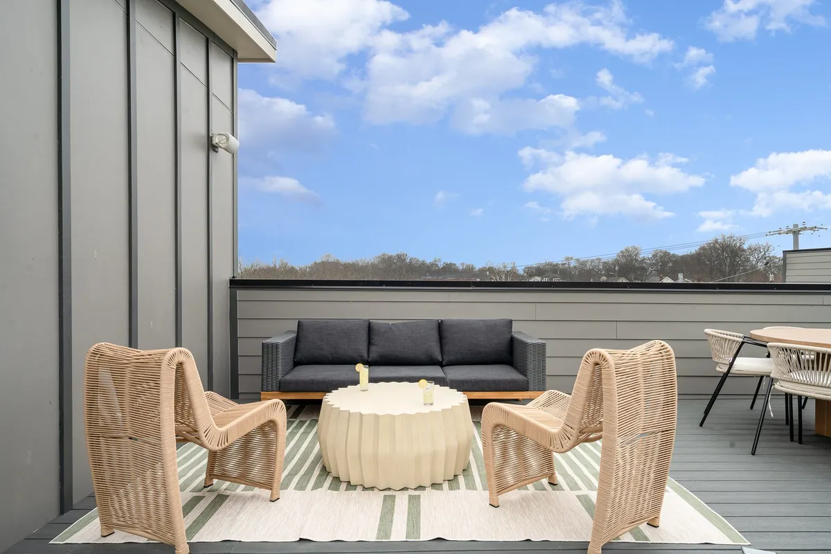 This exterior image captures a cozy rooftop patio setup, featuring a comfortable outdoor sofa, coffee table, rattan chairs, and a stylish rug. The setting is inviting, with ample space for both relaxing and socializing while enjoying panoramic views—perfect for soaking in sunsets or stargazing at night.